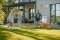 Eine Familie genießt ihren Garten vor einem modernen Haus, in dem eine Luft-Wasser-Wärmepumpe an der Wand installiert ist.